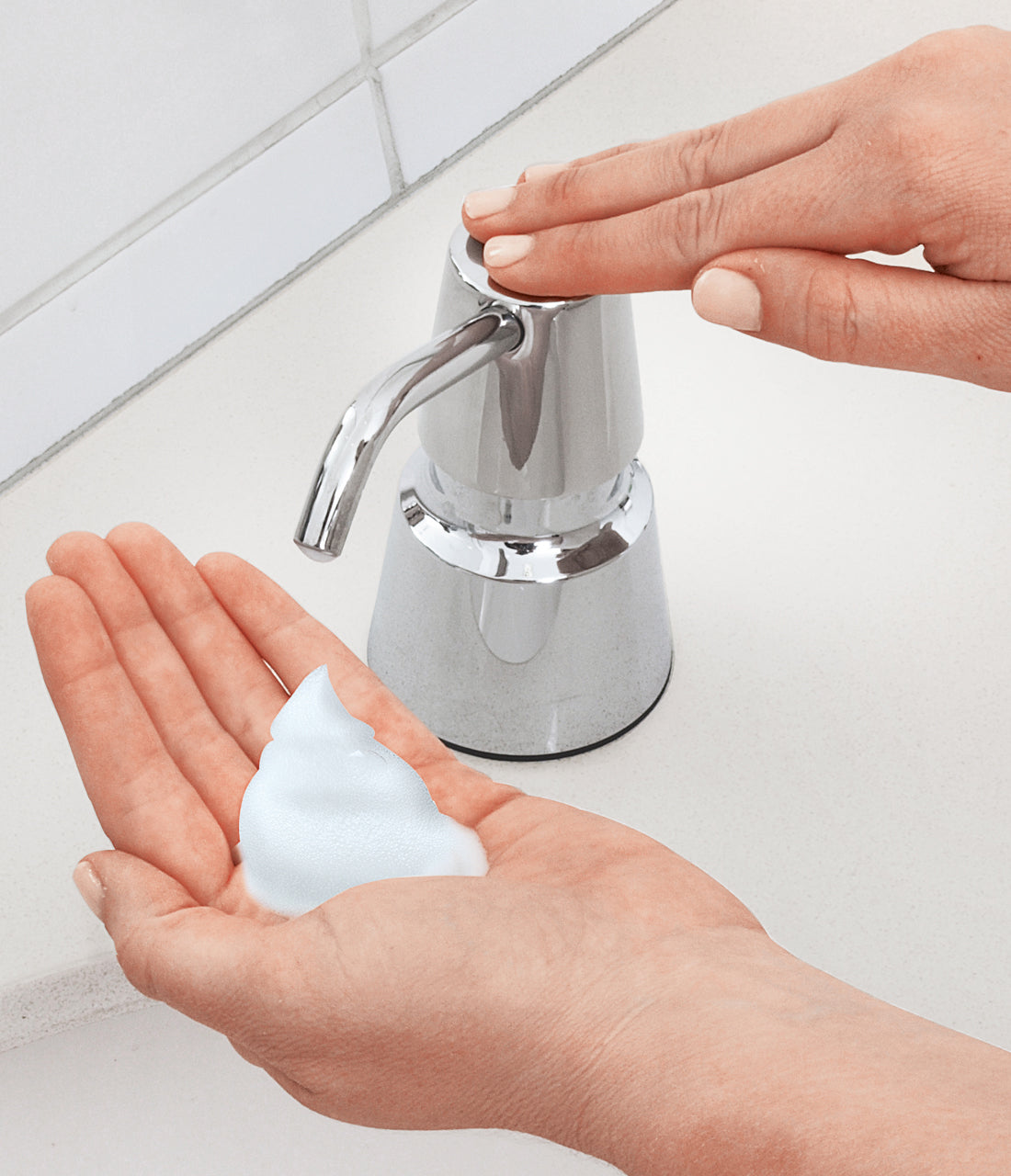 A hand under the Bobrick B-8231 foaming soap dispenser with some foam soap in it.